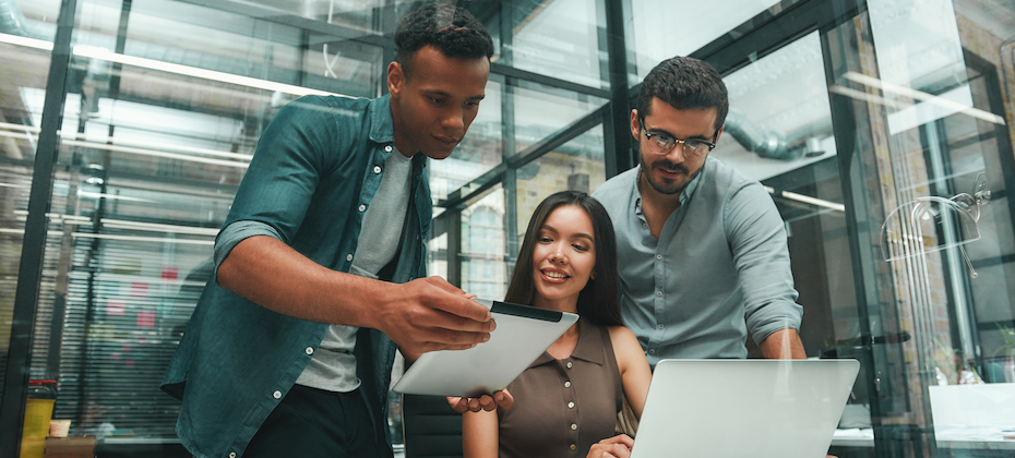 Group of three young and positive employees using modern technologies and discussing something while working in modern office.