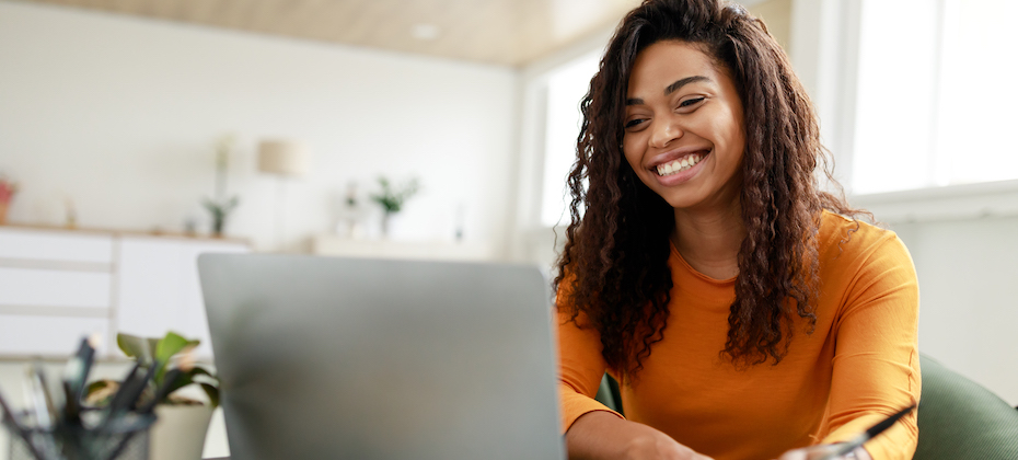 Woman sitting at desk, using computer and writing in notebook