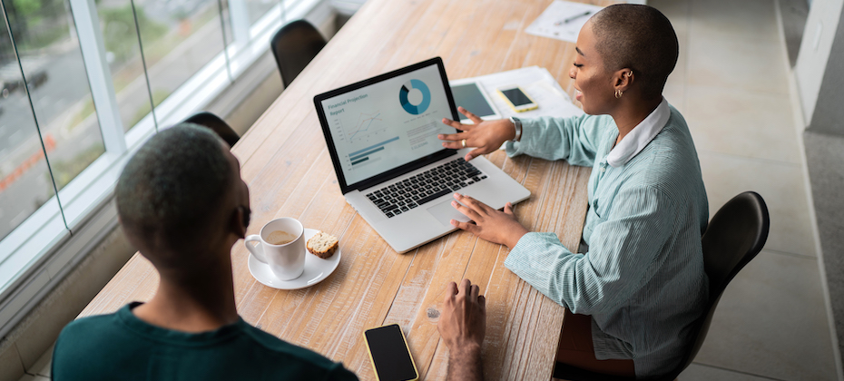 Two Black adults reviewing data on a laptop over coffee