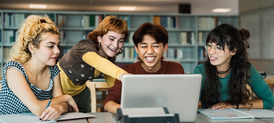 Four young adults use a laptop to study credit and personal finance in a library.