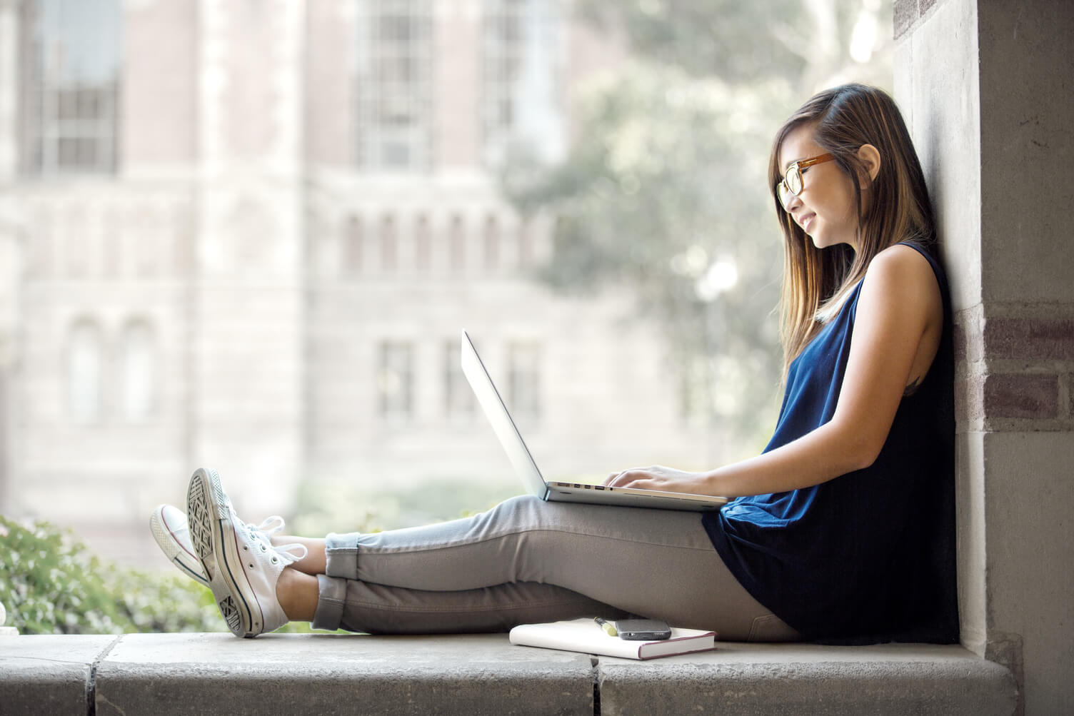 Woman sitting on a ledge looking at a laptop