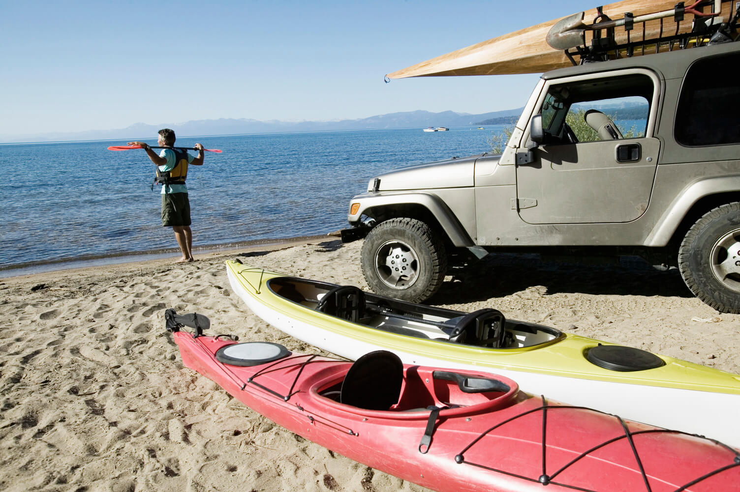 Kayaker look out at the ocean with kayaks and utility vehicle on the beach.