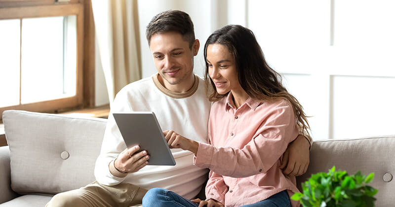 man and woman sitting on couch looking at tablet