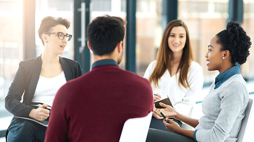 4 multi-ethnic male and female colleagues sitting around in a group talking.