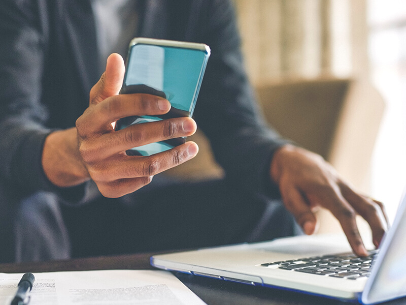 man holding phone using multi factor authentication solutions to login to laptop