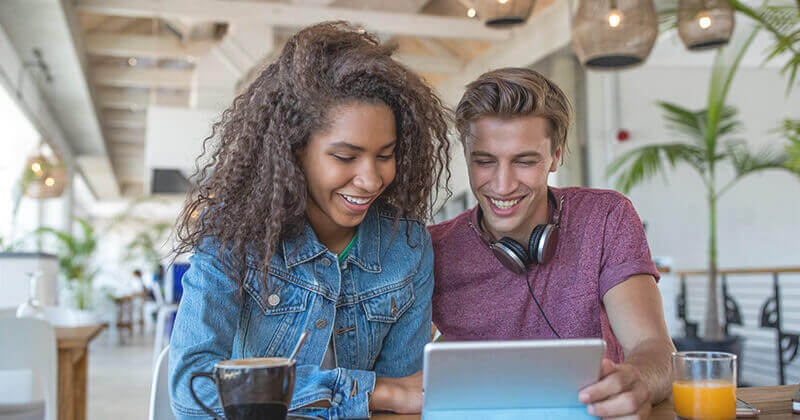 Smiling friends sharing tablet in cafe