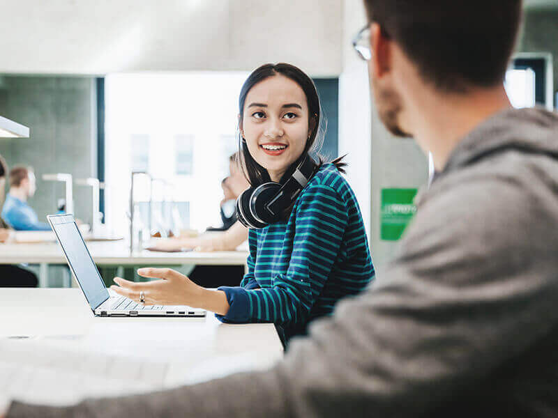 Two students talking while working in library