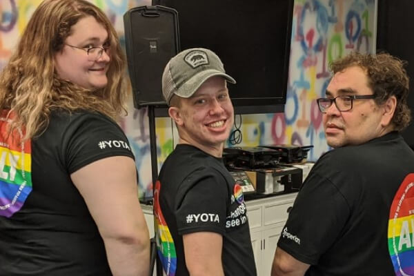 Charlie stands gleefully with his coworkers, donning pride gear 