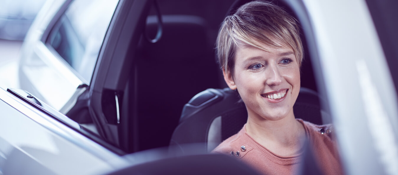 Young white woman cheerfully sitting in the front seat of the right side of a car.