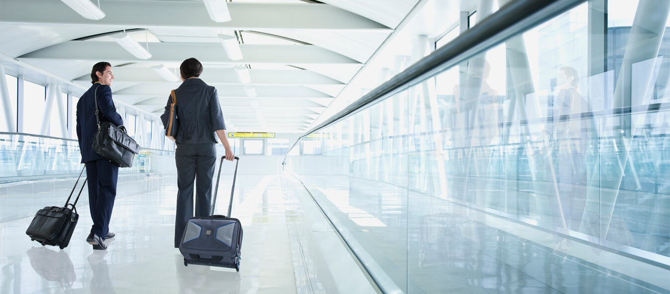 Two travelers walking down a terminal walkway with their luggages in hand.