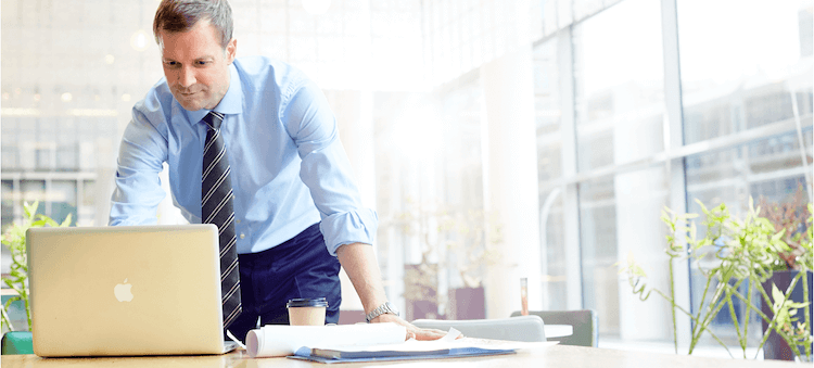 man leaning over desk looking at laptop computer