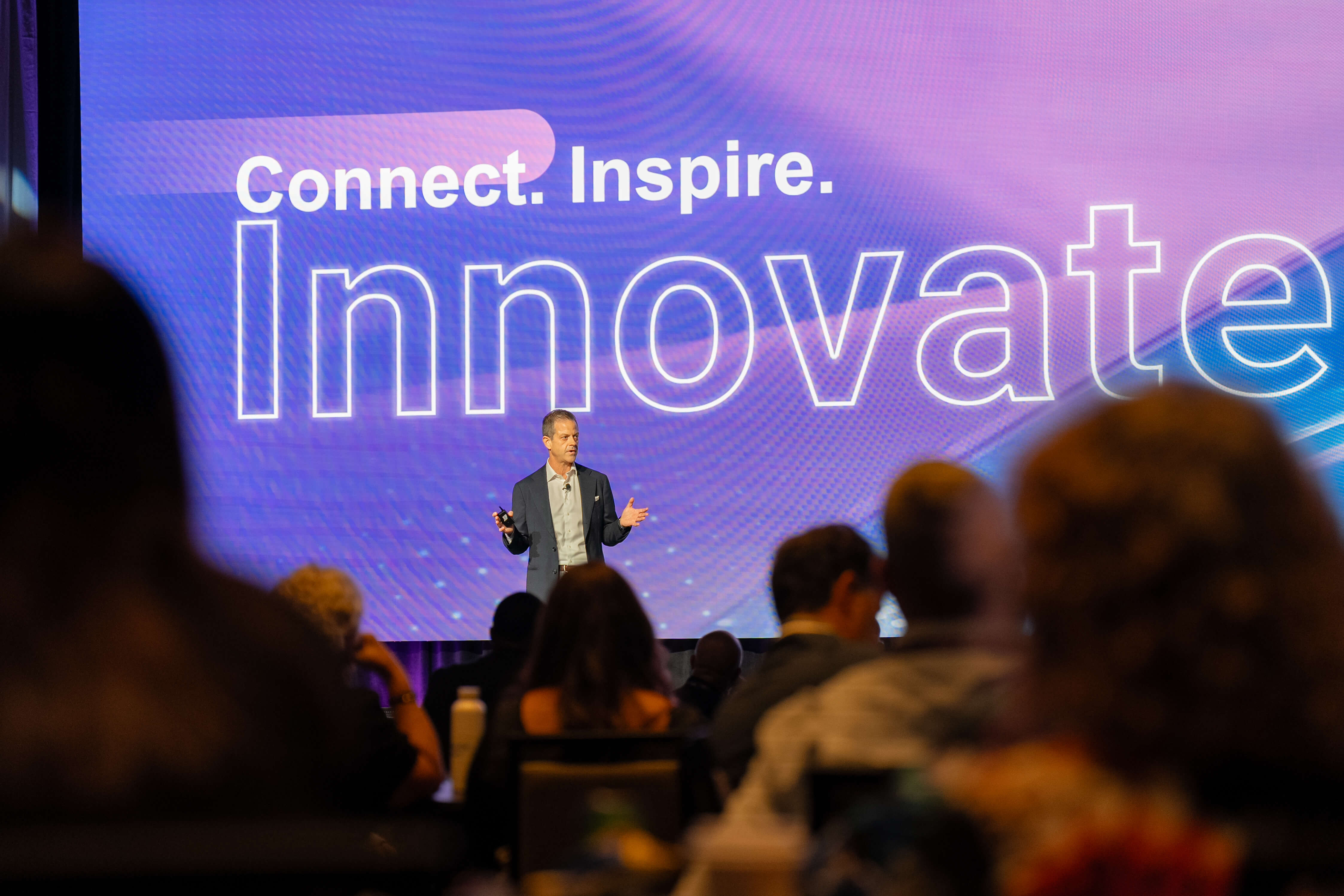 Stage with male speaker. Words behind him say, "Connect. Inspire. Innovate."