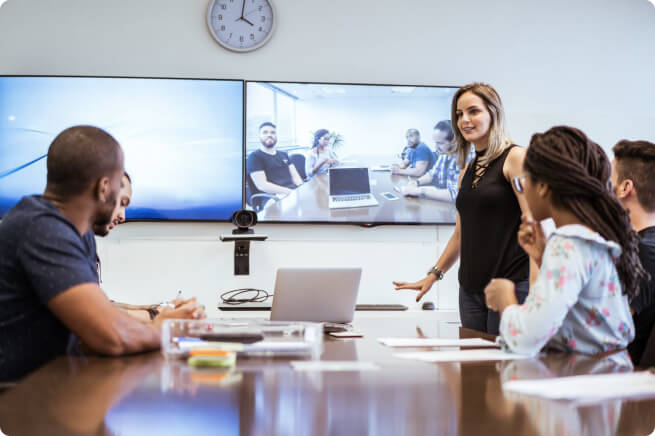 A group of employees have a video meeting with another team in a conference room.
